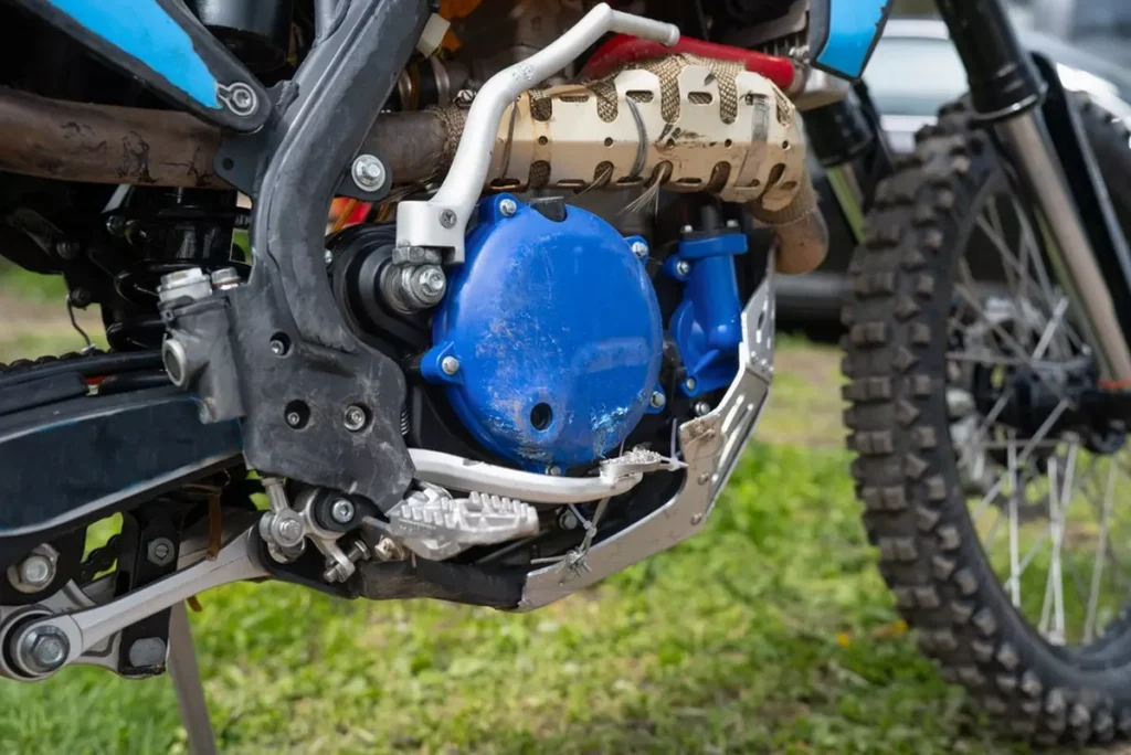 Detailed close-up of a modern dirt bike engine with blue clutch cover and protective aluminum skid plate, off-road motorcycle technical parts.