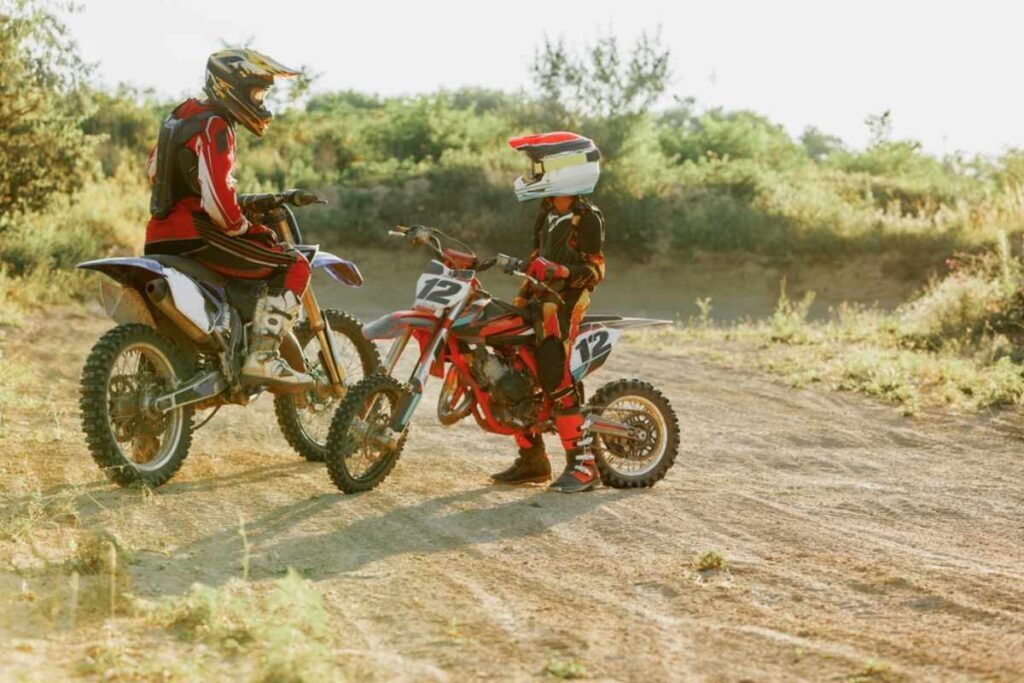 Kid riding a dirt bike on a dirt track with their parent 